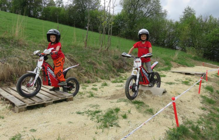 Die zwei Kinder fahren über zwei Verschiedene Hindernisse neben einander mit den Elektro Trial der Marke Oset.